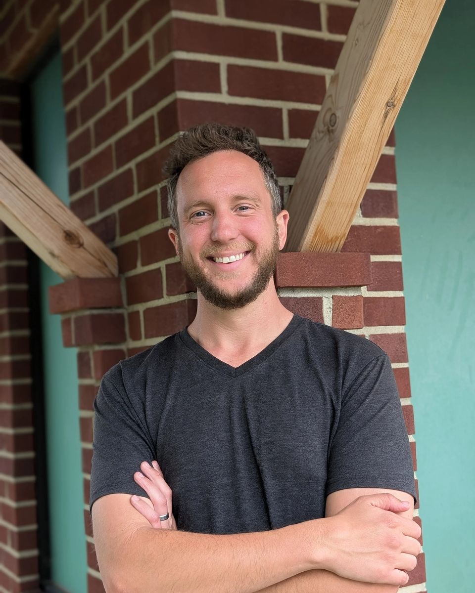 Tim Hickle, smiling with arms crossed in front of a brick wall